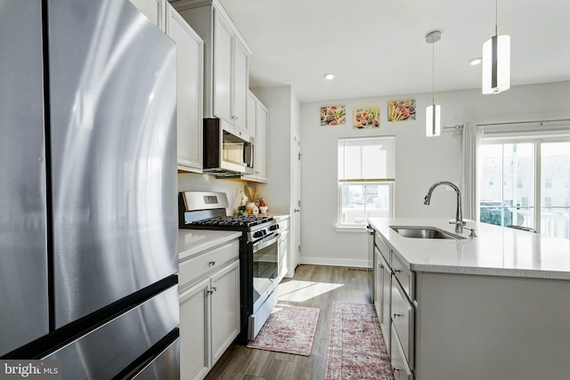 kitchen featuring white cabinets, dark wood-style flooring, hanging light fixtures, stainless steel appliances, and a sink