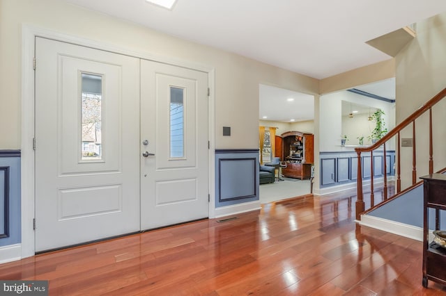 foyer entrance with visible vents, stairway, a decorative wall, and wood finished floors