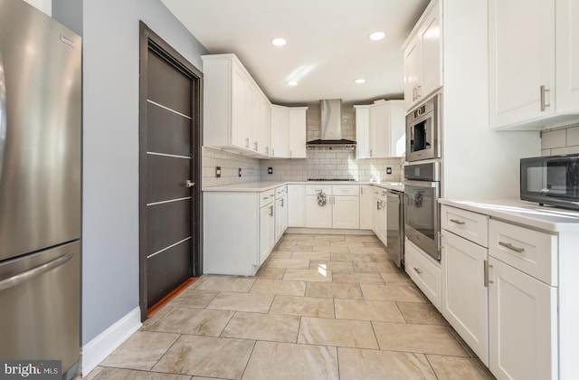 kitchen with light countertops, decorative backsplash, appliances with stainless steel finishes, white cabinetry, and wall chimney range hood