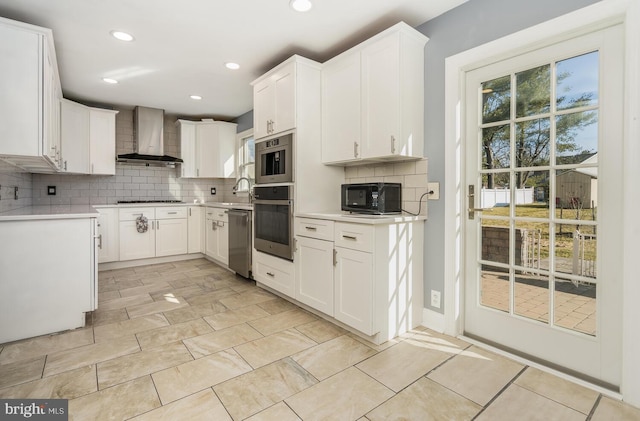 kitchen with wall chimney exhaust hood, stainless steel appliances, backsplash, and light countertops