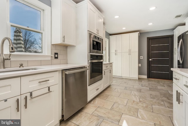 kitchen featuring stainless steel appliances, light countertops, a sink, and tasteful backsplash