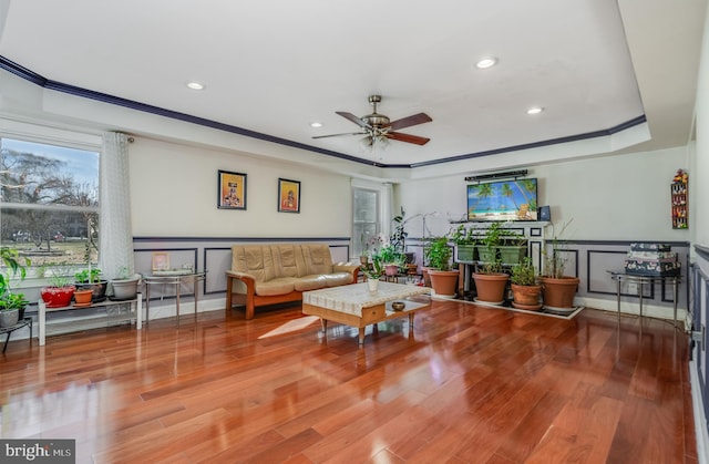 living room with crown molding, a tray ceiling, wood finished floors, and a decorative wall