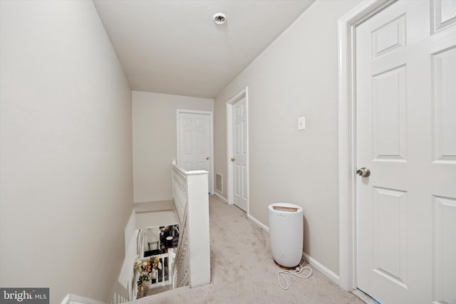 corridor featuring baseboards, light colored carpet, visible vents, and an upstairs landing