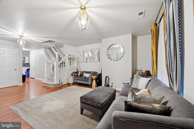 living room featuring stairs, visible vents, baseboards, and wood finished floors