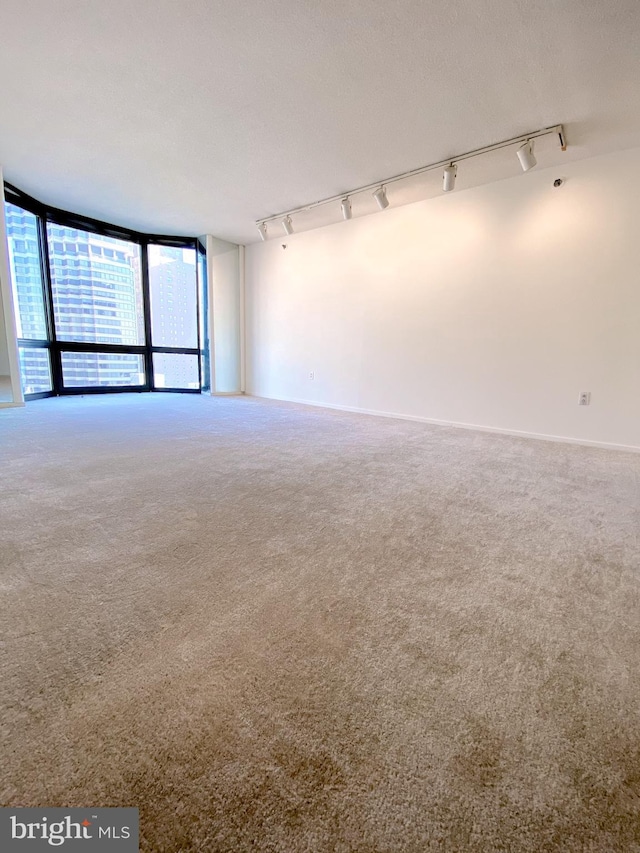 empty room with a textured ceiling, carpet floors, a wall of windows, and baseboards