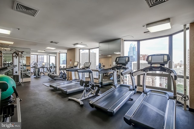 exercise room featuring a view of city, a wall of windows, visible vents, and a healthy amount of sunlight