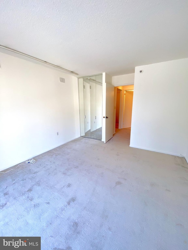 spare room with visible vents, a textured ceiling, and light colored carpet