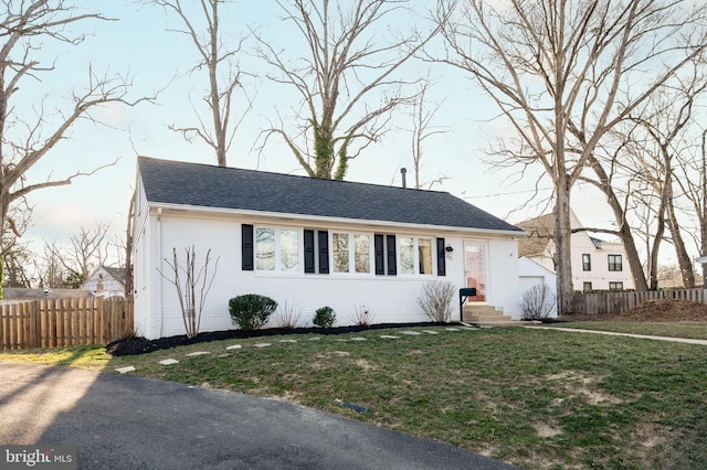 view of front of house with brick siding, roof with shingles, a front yard, and fence