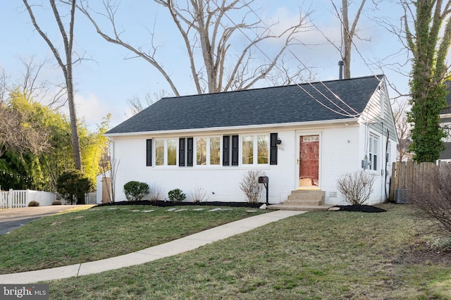 ranch-style house featuring brick siding, roof with shingles, entry steps, fence, and a front lawn