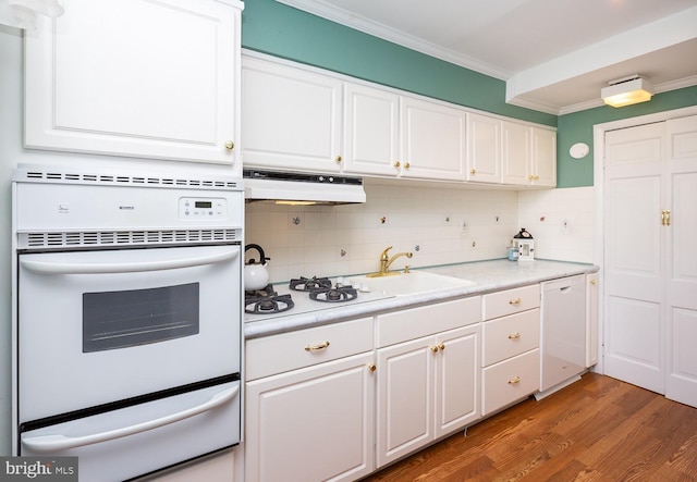 kitchen with under cabinet range hood, white appliances, a sink, ornamental molding, and a warming drawer