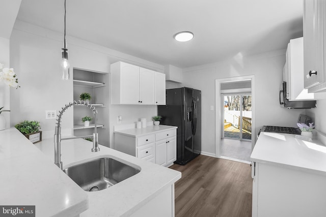 kitchen featuring hanging light fixtures, stove, white cabinetry, a sink, and black fridge