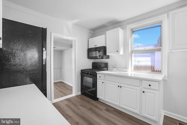 kitchen with black appliances, light countertops, wood finished floors, and white cabinetry