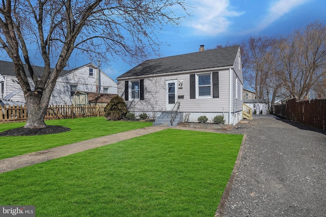 view of front of property with aphalt driveway, fence, a front lawn, and a shingled roof