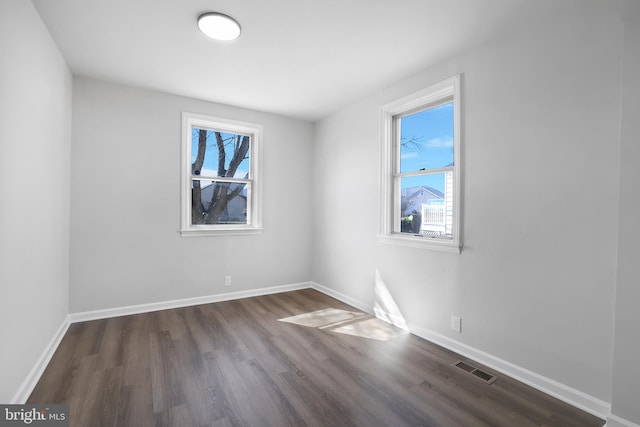 unfurnished room with dark wood-style floors, visible vents, and baseboards