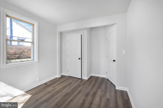 unfurnished bedroom with visible vents, a closet, baseboards, and dark wood-type flooring