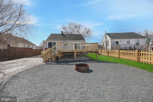 rear view of house with a fire pit, a deck, gravel driveway, and fence