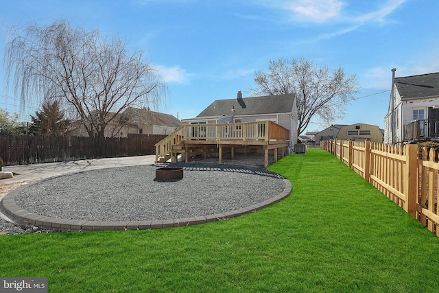 rear view of property featuring a deck, a lawn, a fire pit, and a fenced backyard