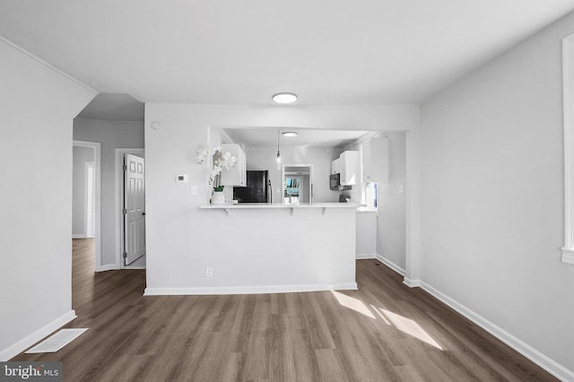 kitchen featuring black appliances, a kitchen bar, white cabinets, and wood finished floors