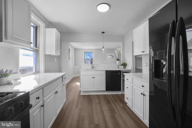 kitchen featuring a peninsula, dark wood-style flooring, a sink, white cabinetry, and black appliances