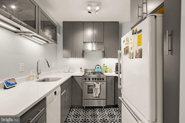 kitchen with gray cabinetry, under cabinet range hood, white appliances, a sink, and light countertops