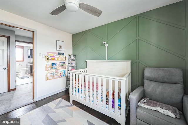 bedroom with ceiling fan, a decorative wall, baseboards, dark wood-style floors, and a crib