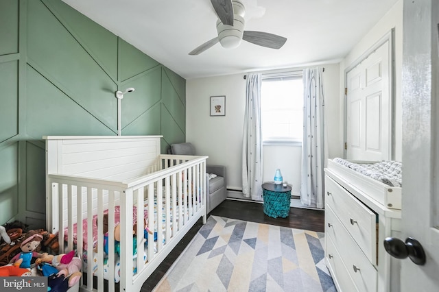 bedroom featuring a nursery area, dark wood finished floors, and a ceiling fan