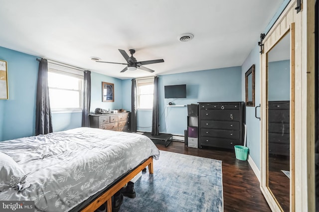 bedroom with ceiling fan, a barn door, dark wood-type flooring, visible vents, and baseboards