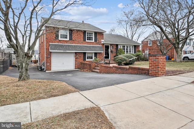 tri-level home with a garage, aphalt driveway, roof with shingles, and brick siding