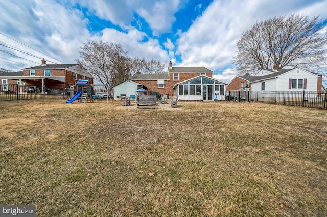 rear view of house featuring a playground, a chimney, a lawn, a sunroom, and a fenced backyard