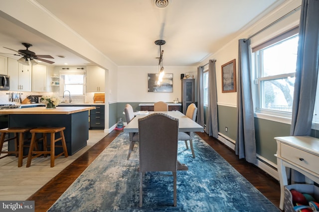 dining area featuring a baseboard radiator, dark wood-type flooring, visible vents, a ceiling fan, and ornamental molding