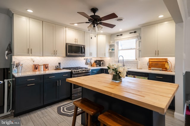 kitchen with a breakfast bar, open shelves, wooden counters, appliances with stainless steel finishes, and white cabinetry