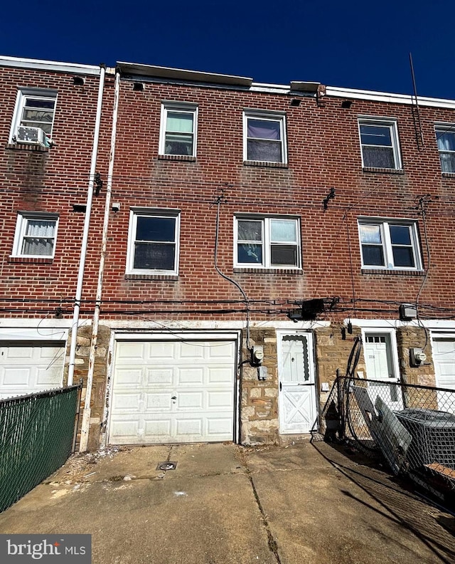 multi unit property featuring a garage, stone siding, brick siding, and fence