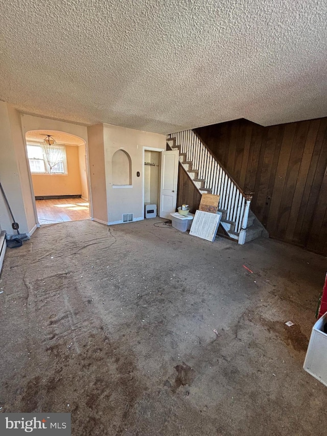 unfurnished living room with wooden walls, visible vents, stairway, and a textured ceiling