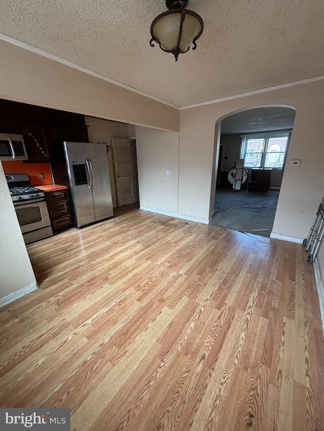 kitchen with arched walkways, a textured ceiling, appliances with stainless steel finishes, light wood-type flooring, and crown molding