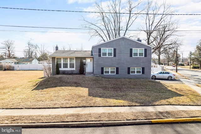 split level home featuring a front yard, fence, and a chimney