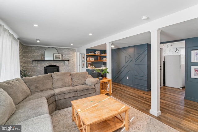 living area with recessed lighting, a brick fireplace, brick wall, and wood finished floors