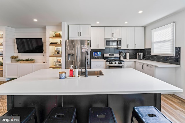 kitchen with a breakfast bar area, light countertops, decorative backsplash, appliances with stainless steel finishes, and white cabinets