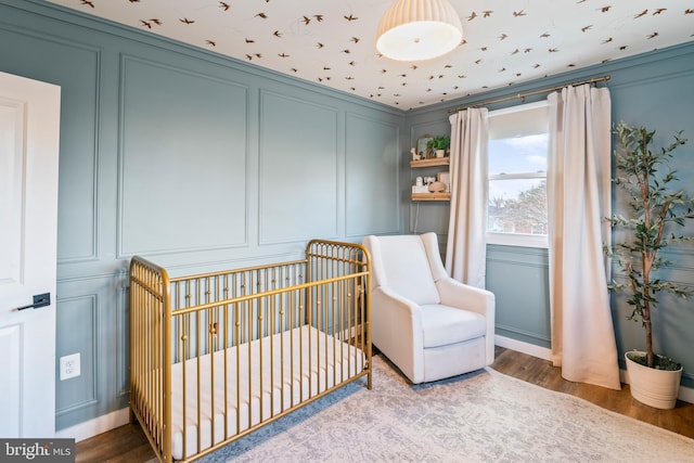 bedroom featuring a nursery area, wood finished floors, and a decorative wall