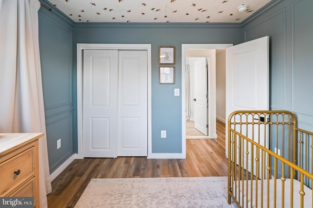 bedroom featuring a crib, a closet, dark wood finished floors, and baseboards