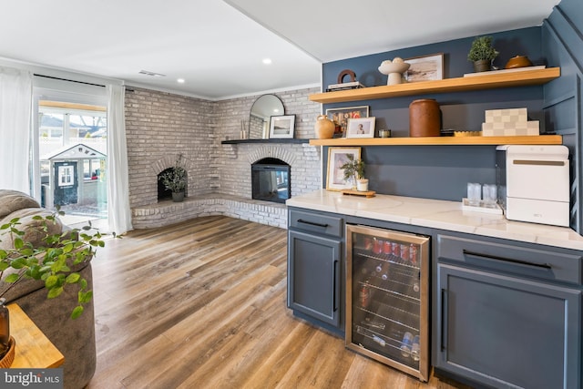 bar featuring beverage cooler, brick wall, light wood-style floors, a brick fireplace, and a dry bar