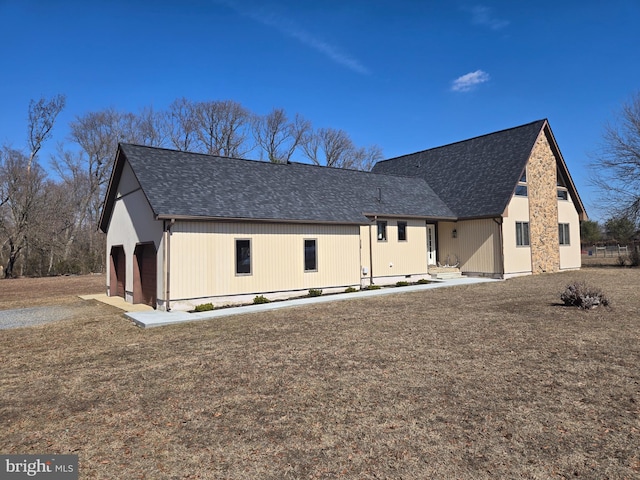 rear view of house featuring a shingled roof and a lawn