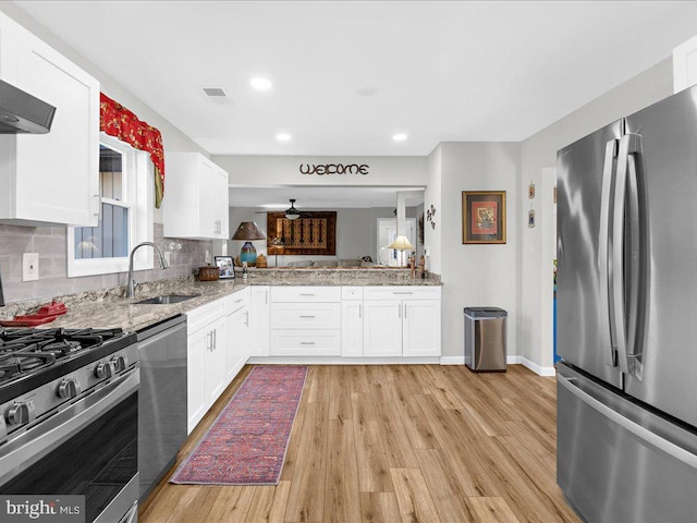 kitchen featuring appliances with stainless steel finishes, white cabinetry, a sink, light stone countertops, and light wood-type flooring