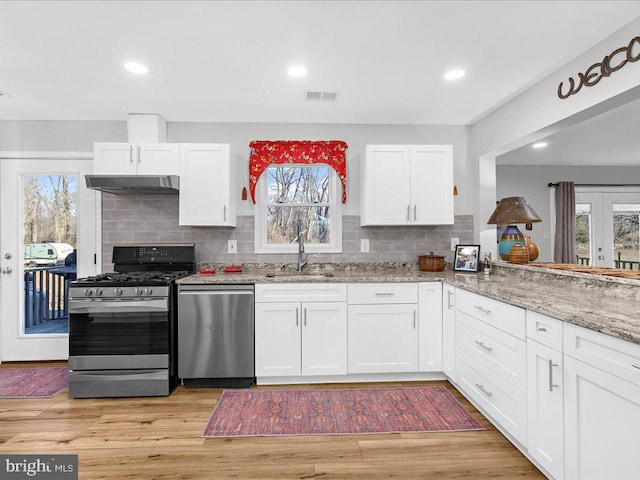 kitchen with light stone counters, under cabinet range hood, stainless steel appliances, a sink, and visible vents