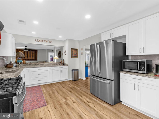 kitchen featuring light wood-type flooring, appliances with stainless steel finishes, decorative backsplash, and a sink