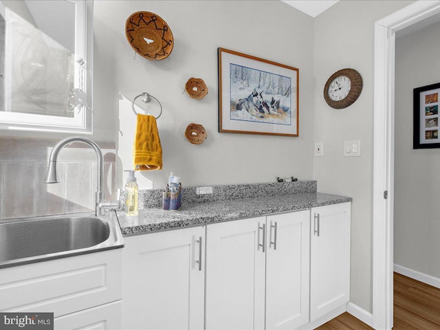 kitchen with wood finished floors, white cabinetry, a sink, light stone countertops, and baseboards