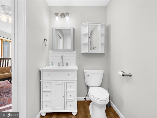 bathroom featuring toilet, wood finished floors, vanity, baseboards, and tasteful backsplash