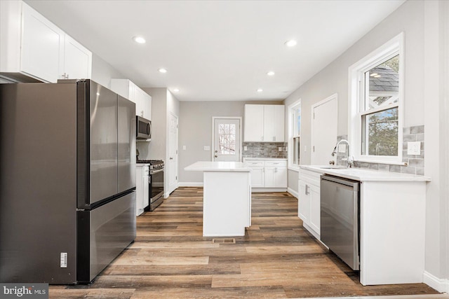 kitchen with stainless steel appliances, wood finished floors, white cabinets, and a center island