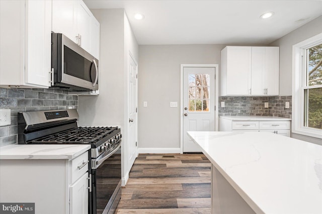 kitchen featuring baseboards, appliances with stainless steel finishes, wood finished floors, and white cabinets