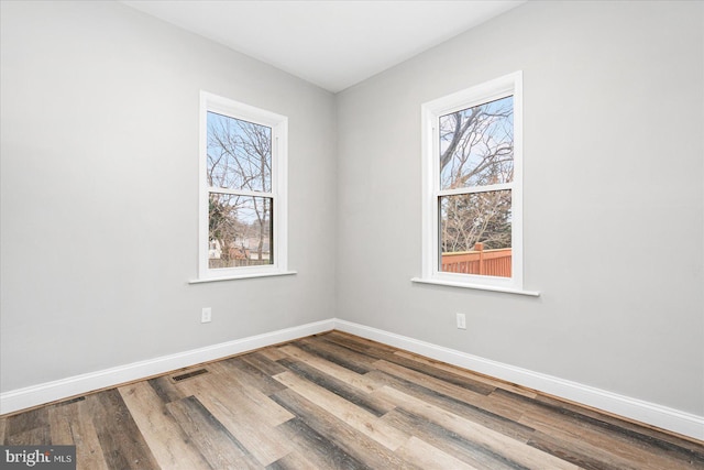 empty room with plenty of natural light, wood finished floors, visible vents, and baseboards