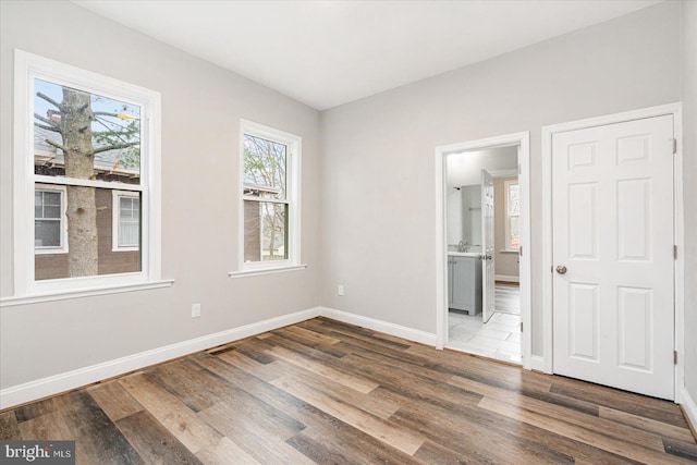 unfurnished bedroom featuring baseboards, wood finished floors, and ensuite bathroom